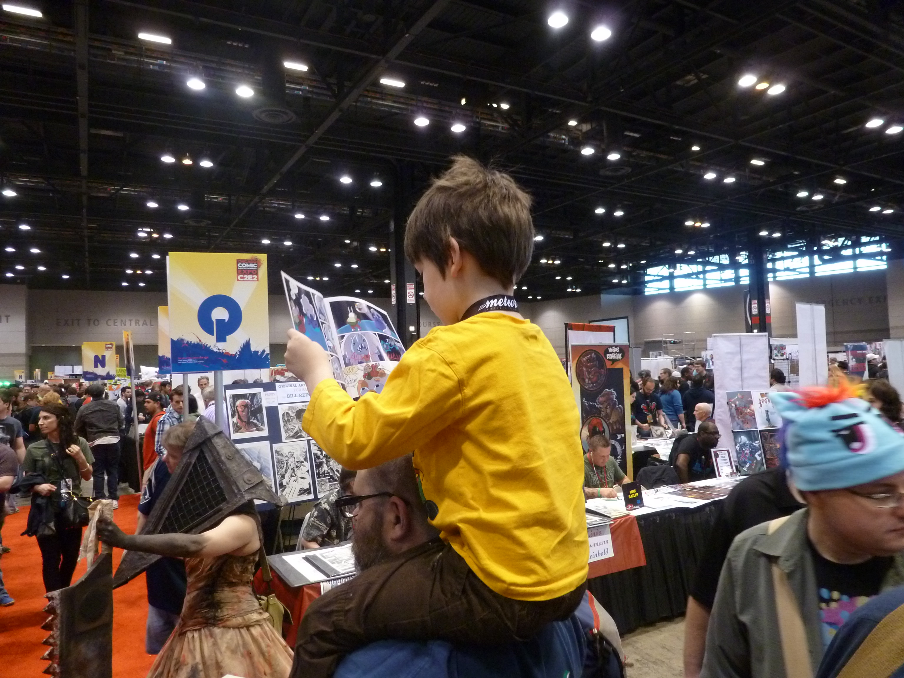 Child at ComicCon riding their parent's shoulders and reading a comic book